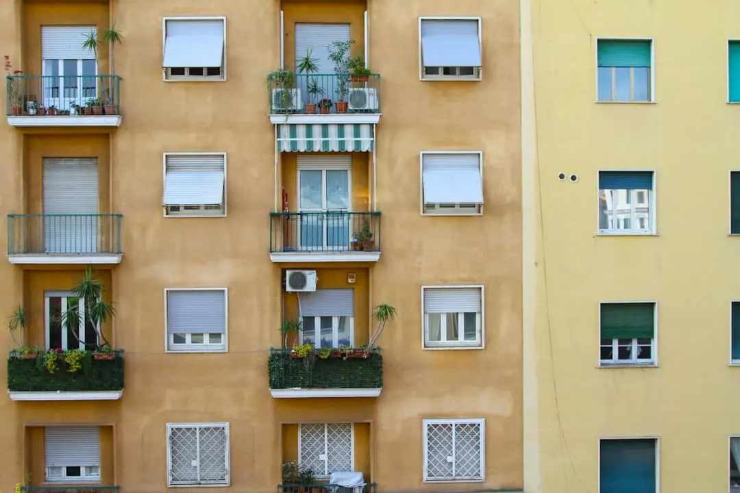Fachada de un bloque de pisos en tonos ocre y amarillo, con balcones llenos de plantas, toldos y persianas