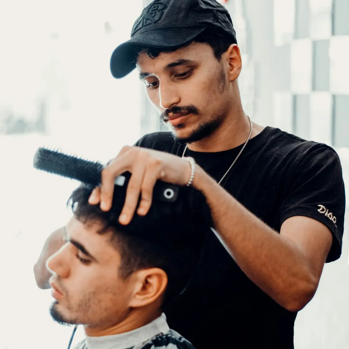 Un barbero con gorra corta el pelo a un cliente sentado en su barbería.