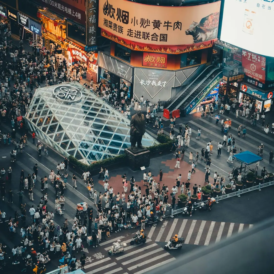 Vista desde lo alto de un cruce lleno de gente en una zona comercial con pantallas y carteles luminosos.