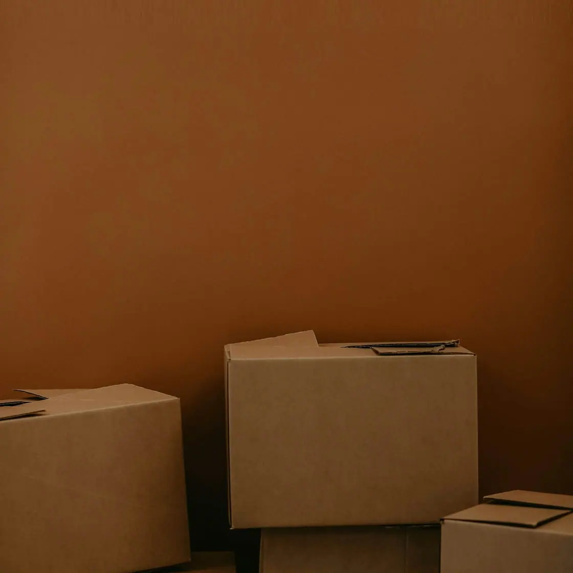 Cajas de cartón de mudanza apiladas contra una pared naranja.