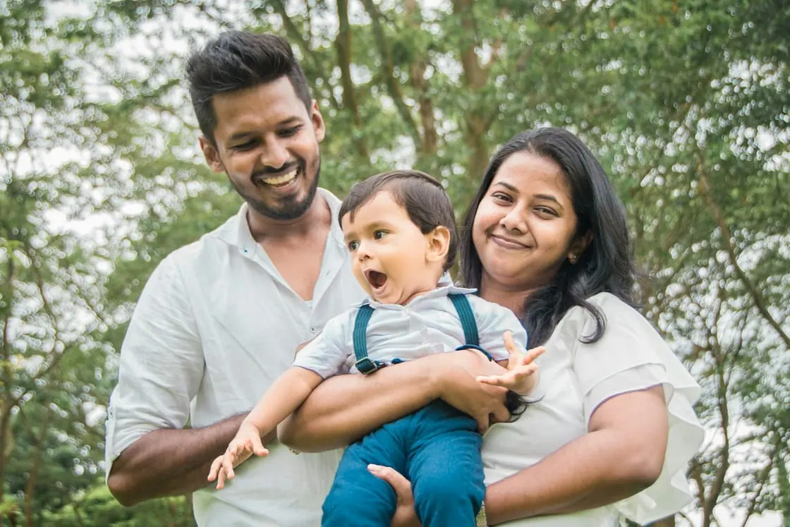 Un padre y una madre sonrientes sostienen a su hijo pequeño en un parque.