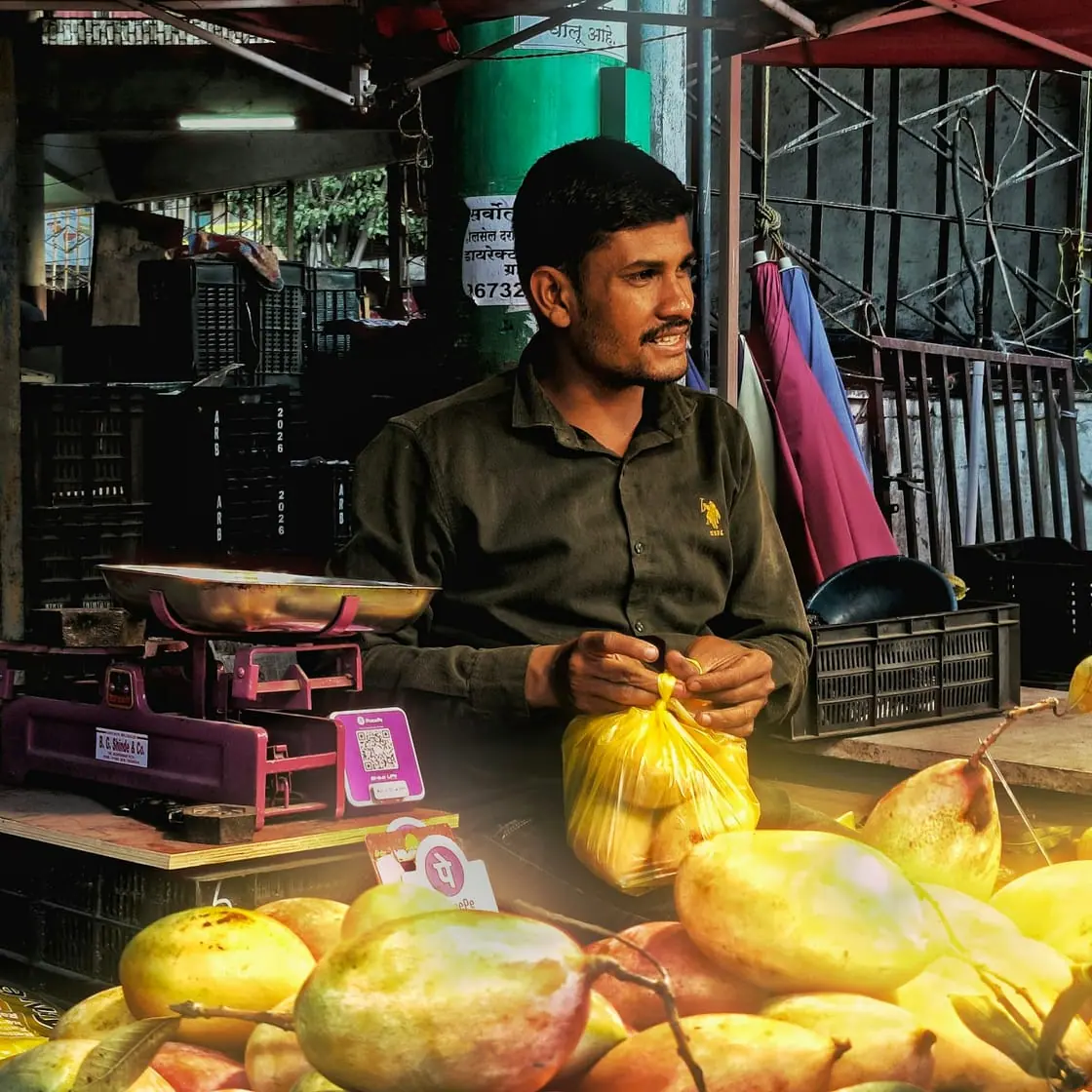 Un vendedor de fruta sentado detrás de su puesto en un mercado, junto a una báscula y un montón de peras.