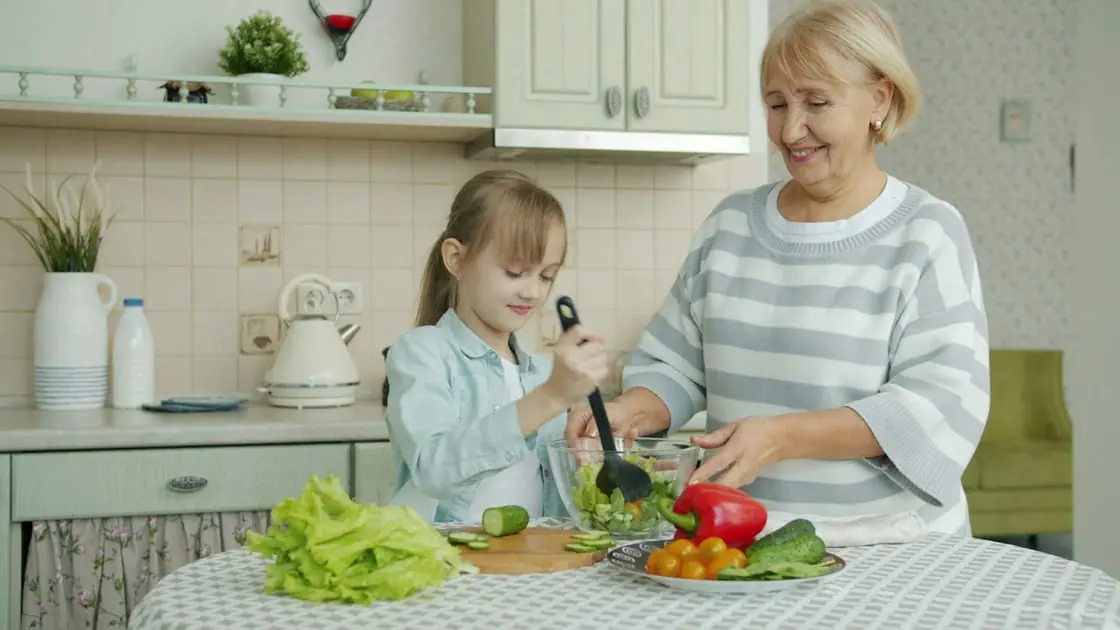 Una abuela y su nieta preparan juntas una ensalada en la mesa de la cocina.