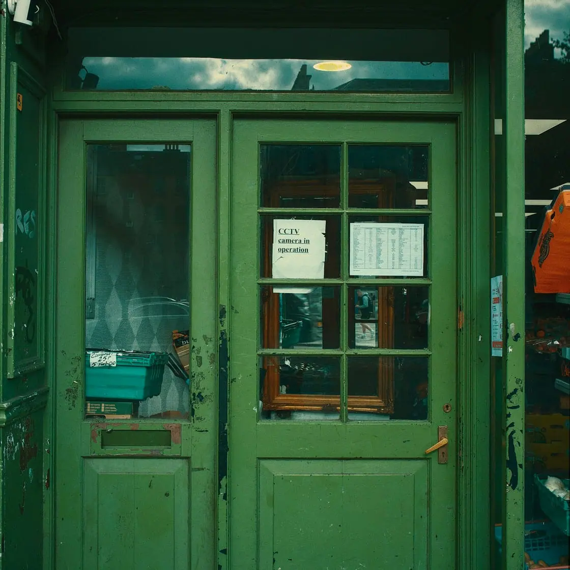 La puerta verde de madera y cristal de una tienda, cerrada.