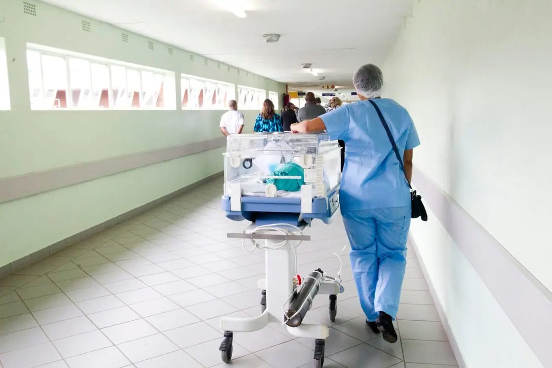 Una enfermera empuja una incubadora por el pasillo luminoso de un hospital.