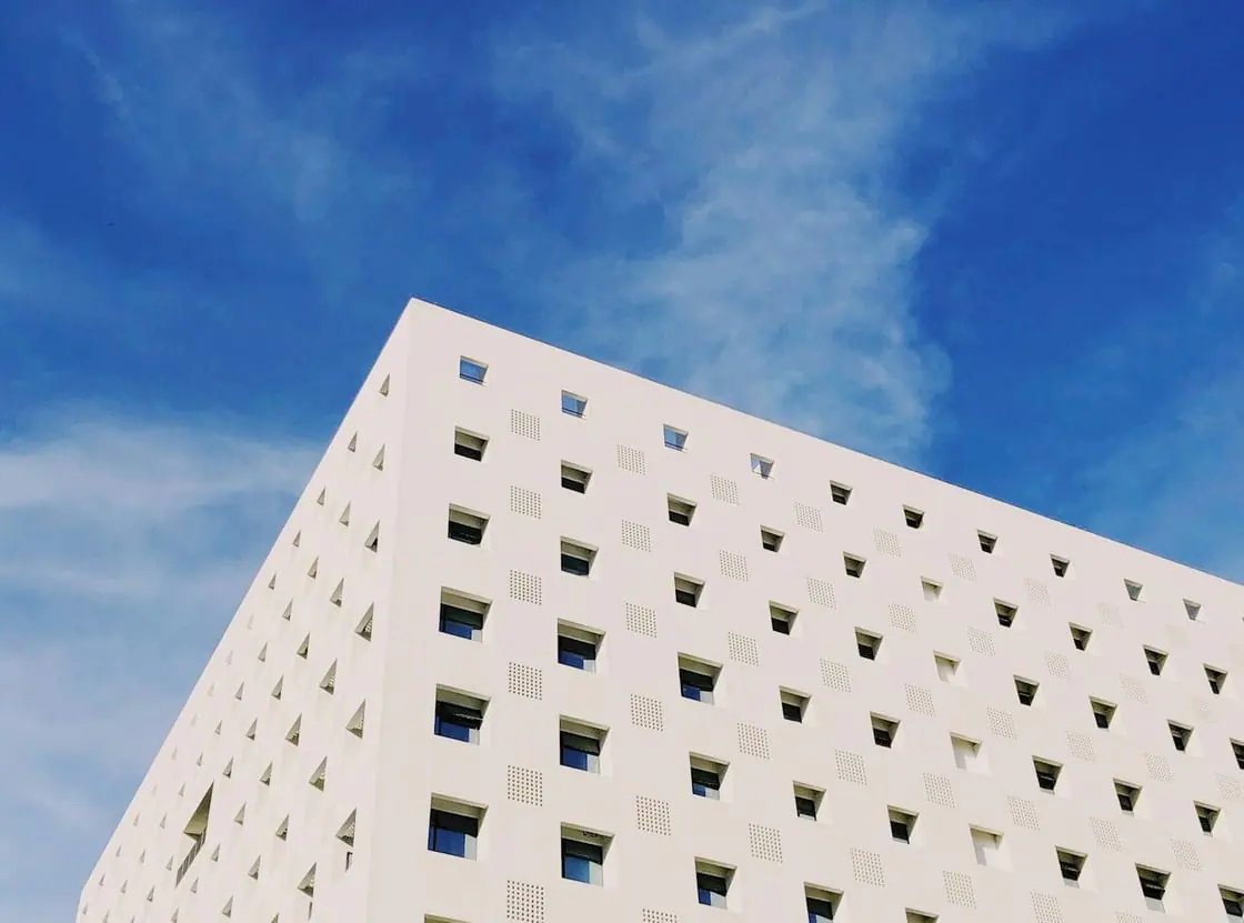 Un edificio blanco lleno de pequeñas ventanas cuadradas, visto desde abajo contra un cielo azul.