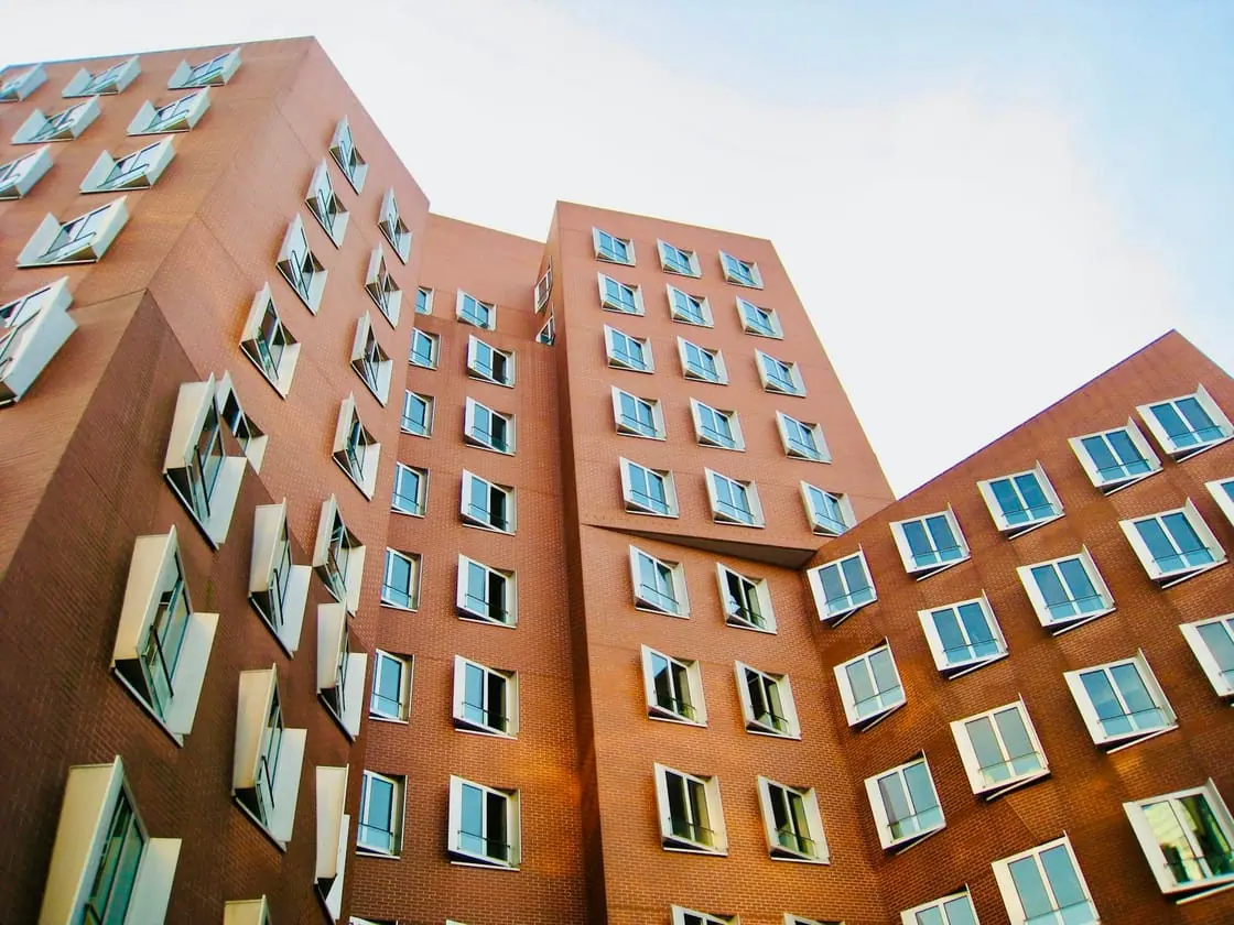 Un edificio de pisos de fachada roja con muchas ventanas, visto desde abajo contra el cielo.