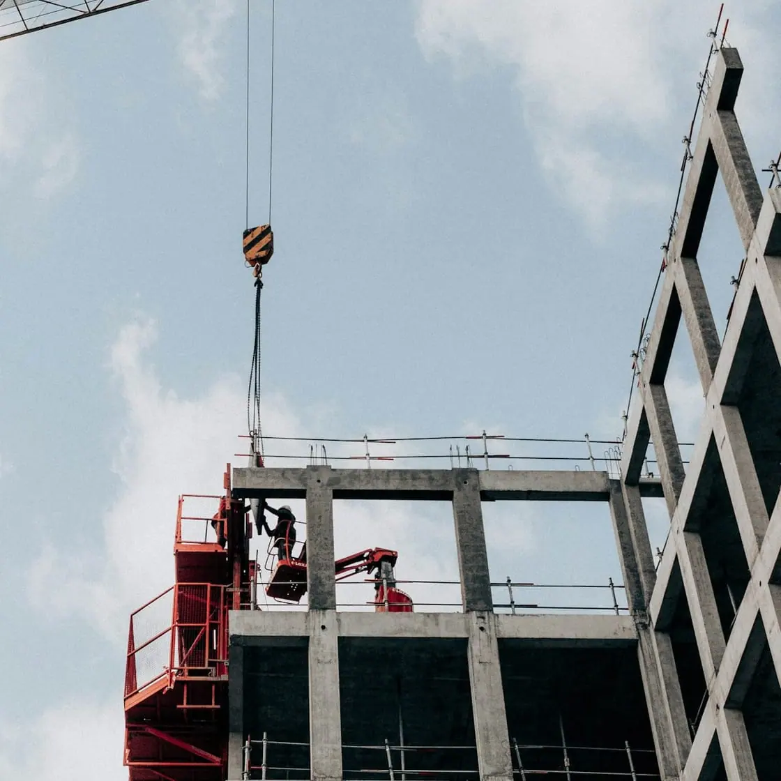 Una grúa junto a la estructura de hormigón de un edificio en obras, vista desde abajo contra el cielo.