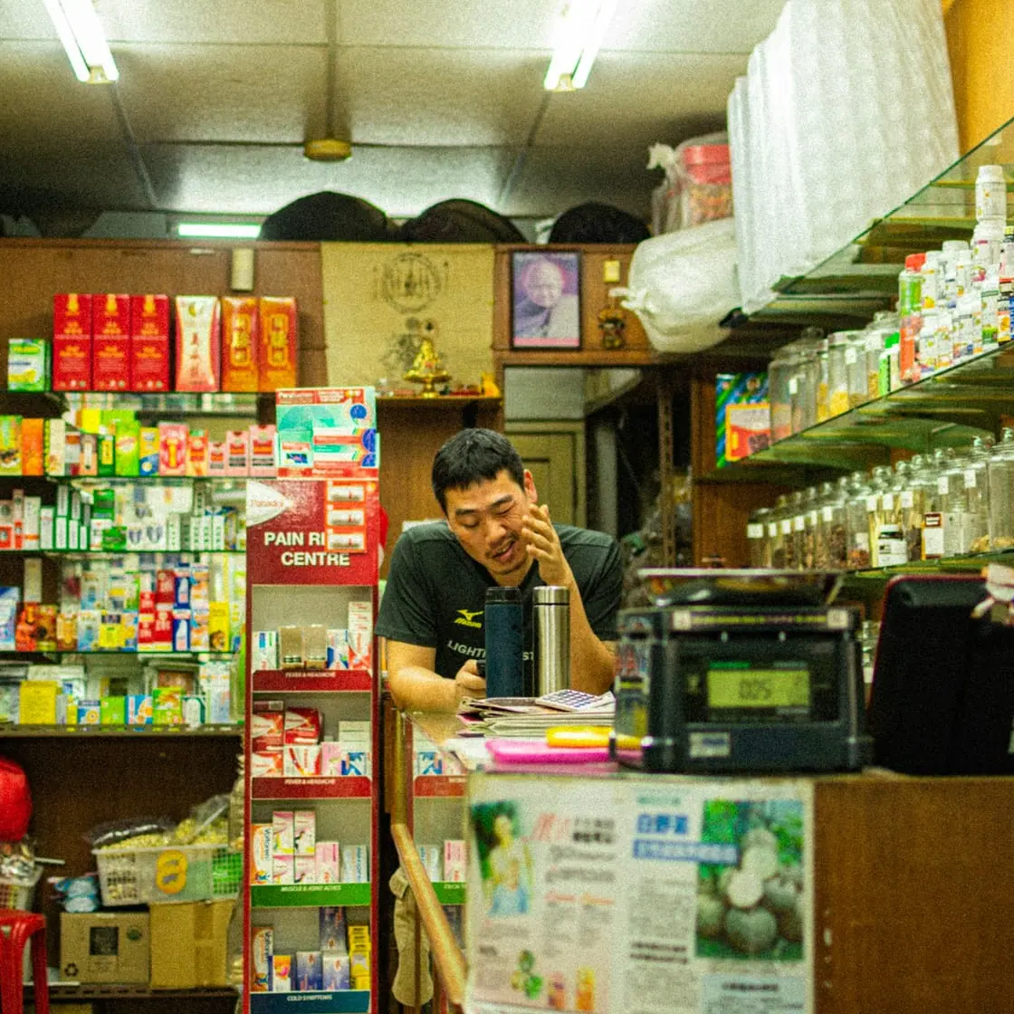 Un tendero atiende tras el mostrador de una pequeña tienda con las estanterías llenas de productos.