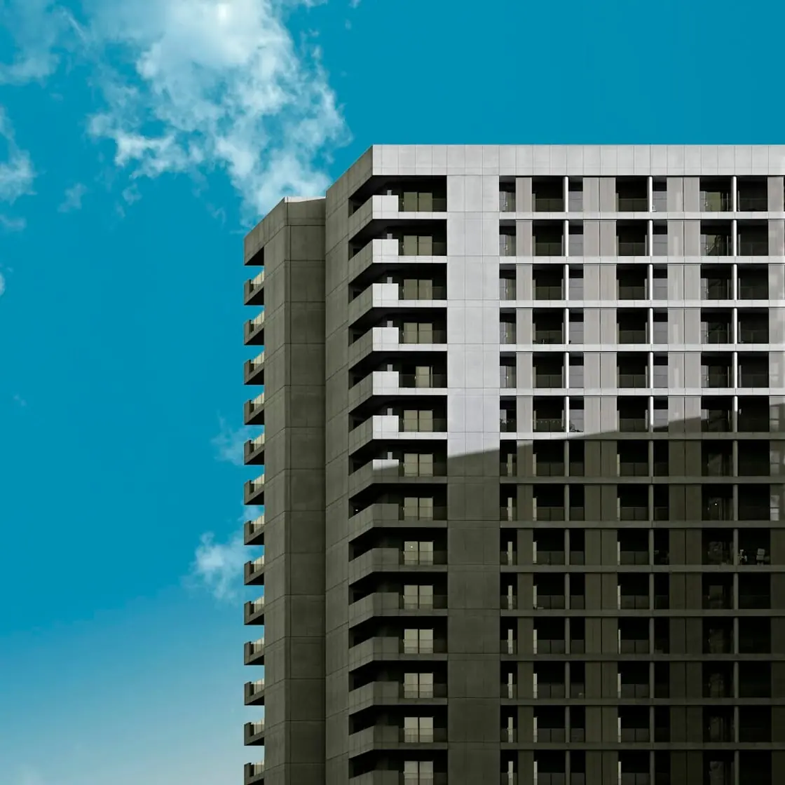 Un edificio alto de viviendas con muchas terrazas contra un cielo azul.