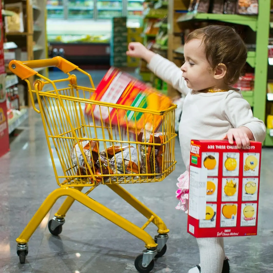 Una niña pequeña empuja un carrito de la compra amarillo en un supermercado.
