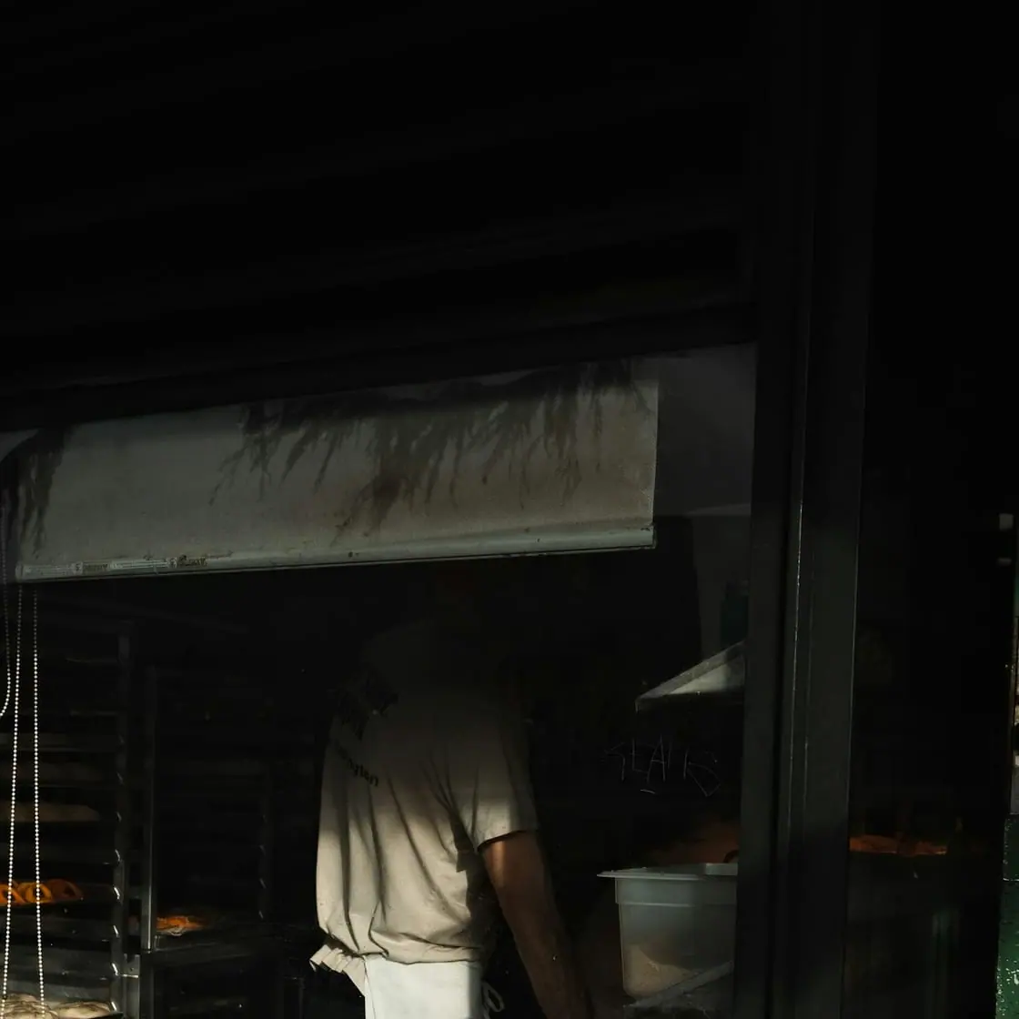 Un panadero saca bandejas de un horno en un obrador en penumbra.