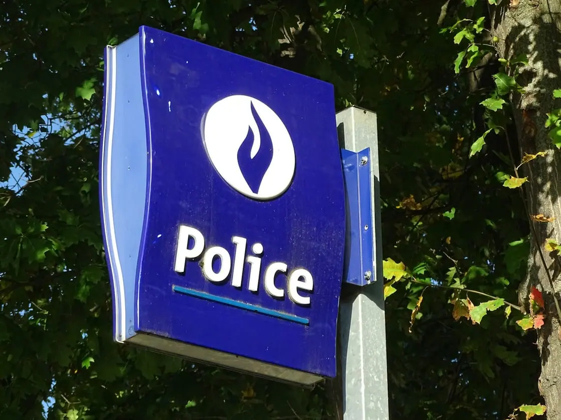 Un cartel azul con la palabra «Police» y un emblema de una llama, entre las hojas de un árbol.