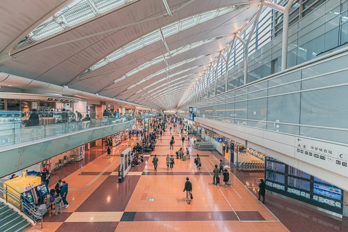 La amplia terminal de un aeropuerto con techo de cristal y viajeros caminando con sus maletas.