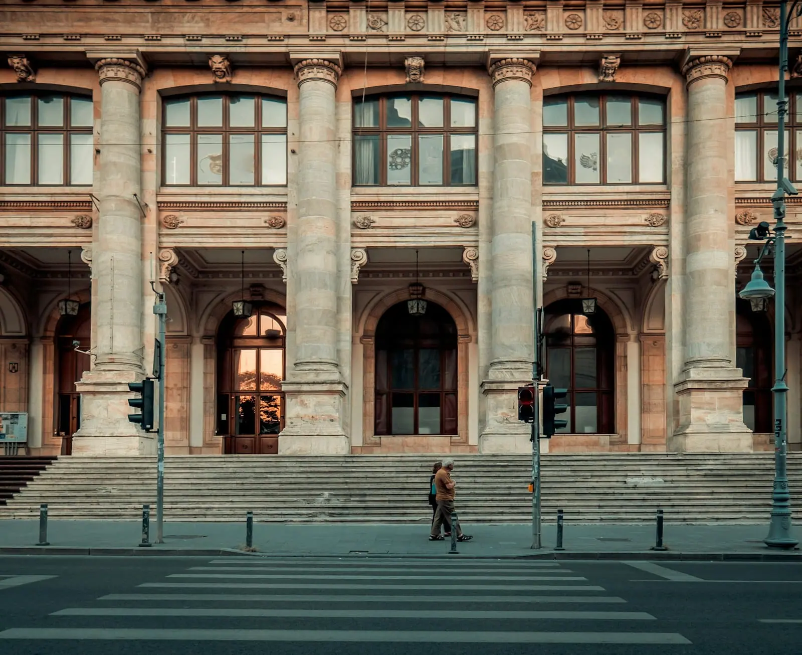 Fachada de un gran edificio público de piedra con columnas y escalinata; una persona cruza la calle por delante.