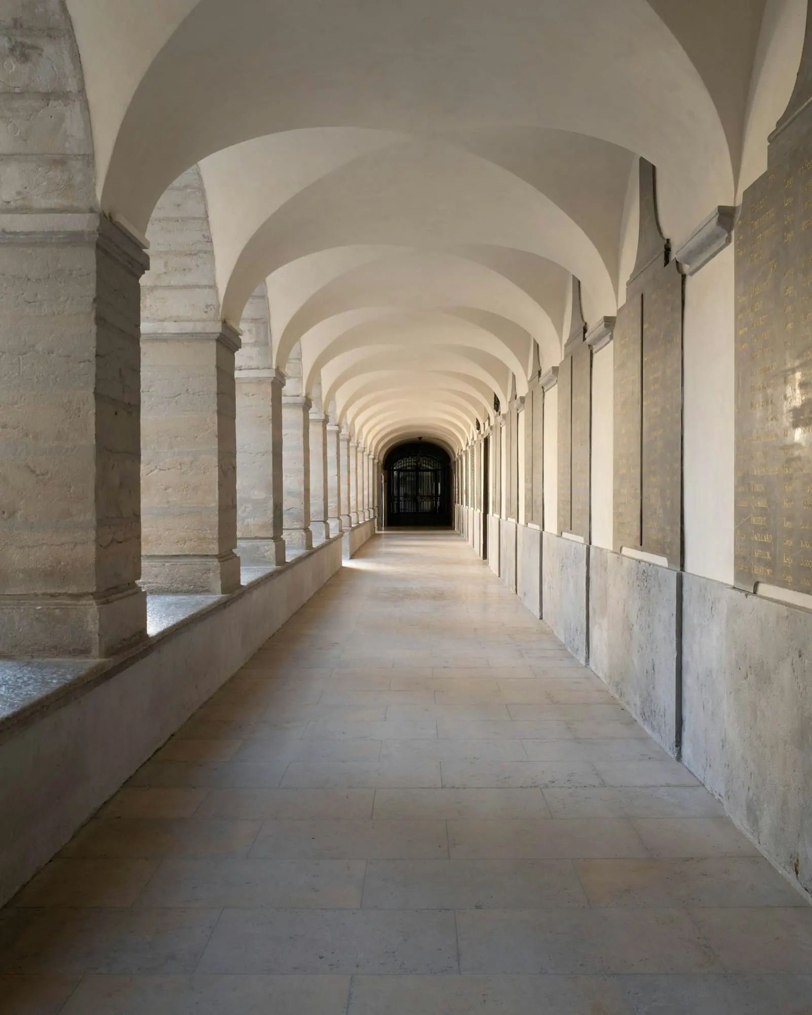 Un largo pasillo con arcos y bóvedas blancas, iluminado por la luz que entra por las ventanas laterales.