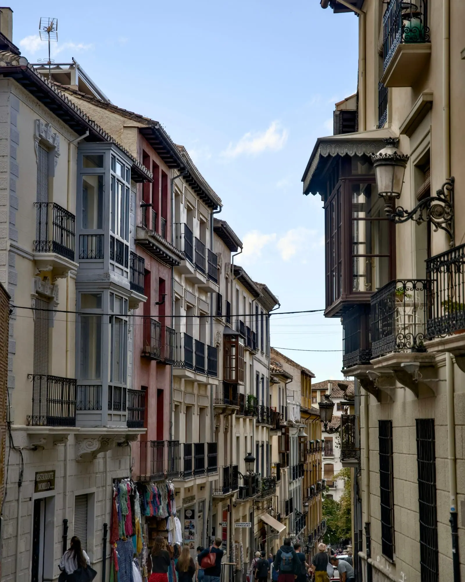 Calle estrecha y empinada de un casco antiguo, con balcones y miradores a ambos lados y gente paseando.